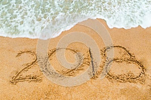 2018 inscription written on sandy beach with wave approaching