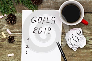 2019 goals on paper note book background and cup of coffee on wood table, business and new year concept