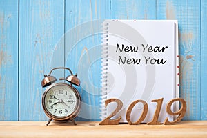 2019 Happy New year New You Text on notebook, retro alarm clock and wooden number on table and copy space