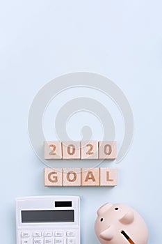 2020 goal, finance plan abstract design concept, wood blocks on blue table background with piggy bank and calculator, top view,