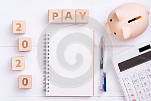 2020 goal, finance plan abstract design concept, wood blocks on white table background with piggy bank and calculator, top view,