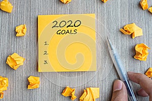 2020 Goal word on yellow note with Businessman holding pen and crumbled paper on wooden table background. New Year New Start,