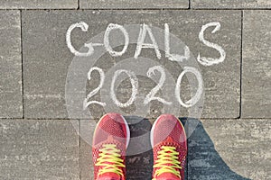 2020 goals, written on gray sidewalk with woman legs in sneakers, top view