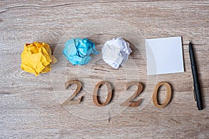 2020 NEW YEAR WITH blank yellow note  and crumbled paper on wooden table background. NEW START, Strategy and Goal concept