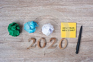 2020 NEW YEAR NEW START word on yellow note with pen and crumbled paper on wooden table background. RESOLUTION, Strategy and Goal