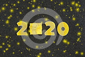 2020 numbers decorated with gold sequins,  ribbon, ball on shiny black background.