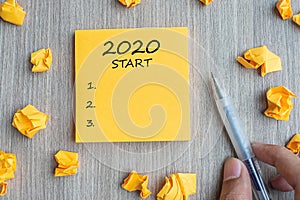 2020 Start word on yellow note with Businessman holding pen and crumbled paper on wooden table background. New Year, Resolutions,