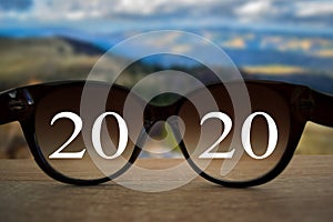 2020 white text with black eye glasses on wooden table over blur autumn landscapes. Business vision happy new year.