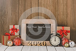 2020 wooden text and Alarm clock with Christmas ornaments and New Year`s Resolutions List written on chalkboard over wooden
