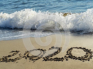 2020 written by hand on the sand beach with beautiful wave and clear blue sea. Handwritten lettering numbers 2020 on sea shore