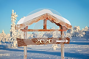 2020 written on a wooden direction sign, blue sky and winter snowy tree landscape background holiday seasons new year greeti