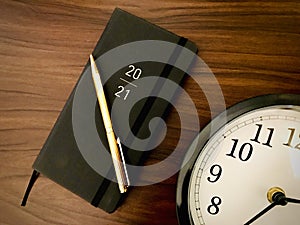 2021 black diary, golden pen, clock, wooden texture background.