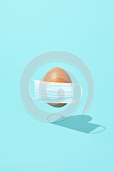 2021 easter egg in surgical mask over blue background. Creative minimal covid easter layout. Health protection, easter, trendy