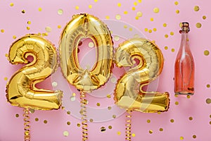 2021 golden air balloon numbers on pink background with bottle of rose champagne wine and confetti. Happy New year eve invitation