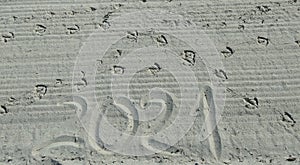 2021 handwritten on sandy beach and Seagull footprints