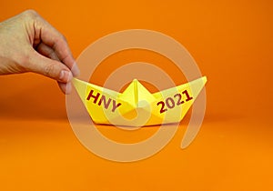 2021 HNY symbol. Image of businessman pushing paper made origami boat forward with words 2021 HNY - Happy New Year. Over orange