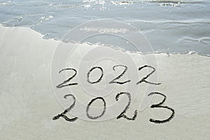 2022 2023  handwritten text  in sand on a beach with waves in an exotic island for future, hope, unity