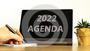 2022 agenda new year symbol. Tablet with words 2022 agenda. Businessman hand with pen, house plant. Copy space. Beautiful white