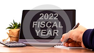 2022 fiscal new year symbol. Tablet with words `fiscal year`. Businessman hand with pen, house plant. Copy space. Beautiful whit