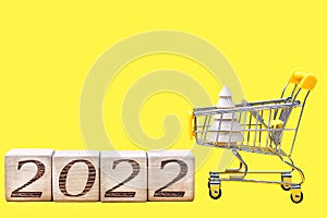 2022 numbers on wooden blocks next to a shopping cart carrying a wooden Christmas tree. The idea of Christmas shopping and