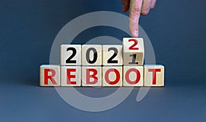 2022 reboot new year symbol. Businessman turns a wooden cube and changes words `Reboot 2021` to `Reboot 2022`. Beautiful grey