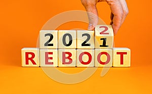 2022 reboot new year symbol. Businessman turns a wooden cube and changes words `Reboot 2021` to `Reboot 2022`. Beautiful orang