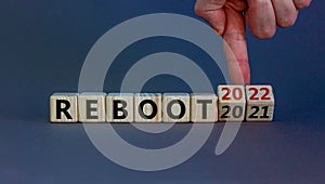 2022 reboot new year symbol. Businessman turns wooden cubes and changes words `Reboot 2021` to `Reboot 2022`. Beautiful grey