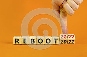 2022 reboot new year symbol. Businessman turns wooden cubes and changes words `Reboot 2021` to `Reboot 2022`. Beautiful orange