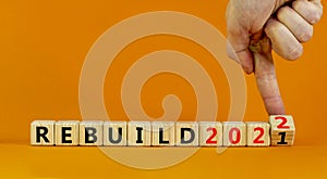 2022 rebuild new year symbol. Businessman turns a wooden cube and changes words `Rebuild 2021` to `Rebuild 2022`. Beautiful or