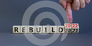 2022 rebuild new year symbol. Businessman turns a wooden cube and changes words `Rebuild 2021` to `Rebuild 2022`. Beautiful gr