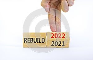 2022 rebuild new year symbol. Businessman turns a wooden cube and changes words `Rebuild 2021` to `Rebuild 2022`. Beautiful wh