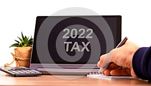 2022 tax new year symbol. Tablet with words `2022 tax`. Businessman hand with pen, house plant. Copy space. Beautiful white