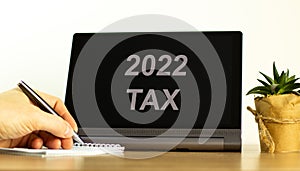 2022 tax new year symbol. Tablet with words `2022 tax`. Businessman hand with pen, house plant. Copy space. Beautiful white