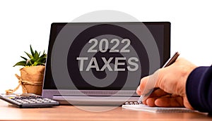2022 taxes new year symbol. Tablet with words `2022 taxes`. Businessman hand with pen, house plant. Copy space. Beautiful white