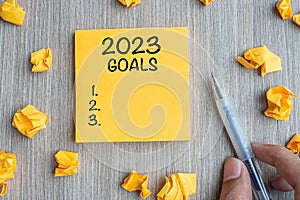 2023 Goal word on yellow note with Businessman holding pen and crumbled paper on wooden table background. New Year New Start,