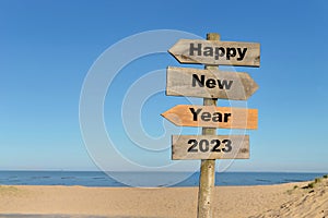 2023 happy new year written on a direction sign in front of a beach