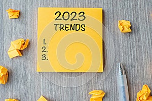 2023 Trends word on yellow note with pen and crumbled paper on wooden table background. New Year New Start, Resolutions, Strategy