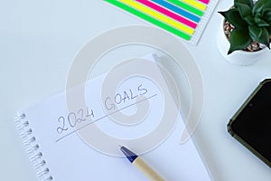 2024 goals, handwritten text in a notebook with pen and smart phone on white background