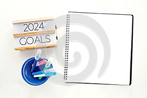 2024 goals on wood box and blank notebook paper on white marble background, business new year aim to success