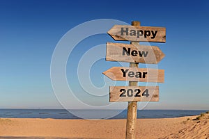 2024 happy new year written on a direction sign in front of a beach