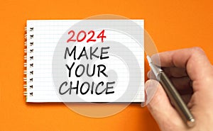 2024 Make your choice symbol. Concept words 2024 Make your choice on beautiful white note. Beautiful orange background. Voter hand