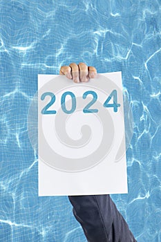 2024, Man holding cardboard with number 2024 on background of faded lights. Happy New Year