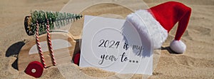 2024 IS MY YEAR TO.. text on paper greeting card on background sandy beach sun coast. Christmas balls Santa hat New Year
