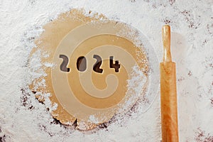 2024 numbers carved on gingerbread dough on white four and rolling pin