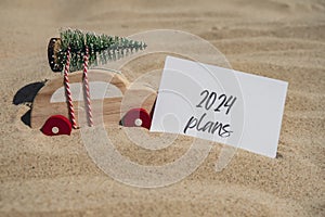 2024 PLANS text on paper greeting card on background sandy beach sun coast. Christmas balls Santa hat New Year New Me