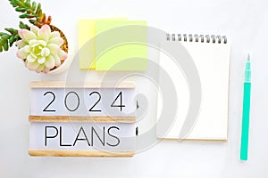 2024 plans on wood box and blank notebook paper on white marble background, business new year aim to success