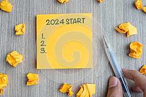 2024 Start word on yellow note with Businessman holding pen and crumbled paper on wooden table background. New Year, Resolutions,