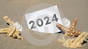 2024 text start new year symbol on paper greeting card on background of starfish summer vacation decor. Sandy beach sun