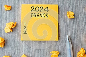 2024 Trends word on yellow note with pen and crumbled paper on wooden table background. New Year New Start, Resolutions, Strategy