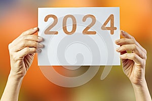 2024, Woman holding cardboard with number 2024 on orange background. Happy New Year